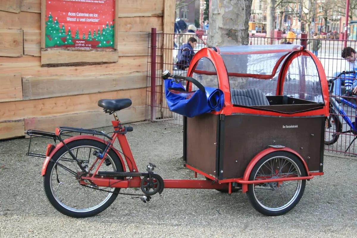 A stationary red cargo bike with a canopy parked on a city street, symbolizing eco-friendly urban transport.