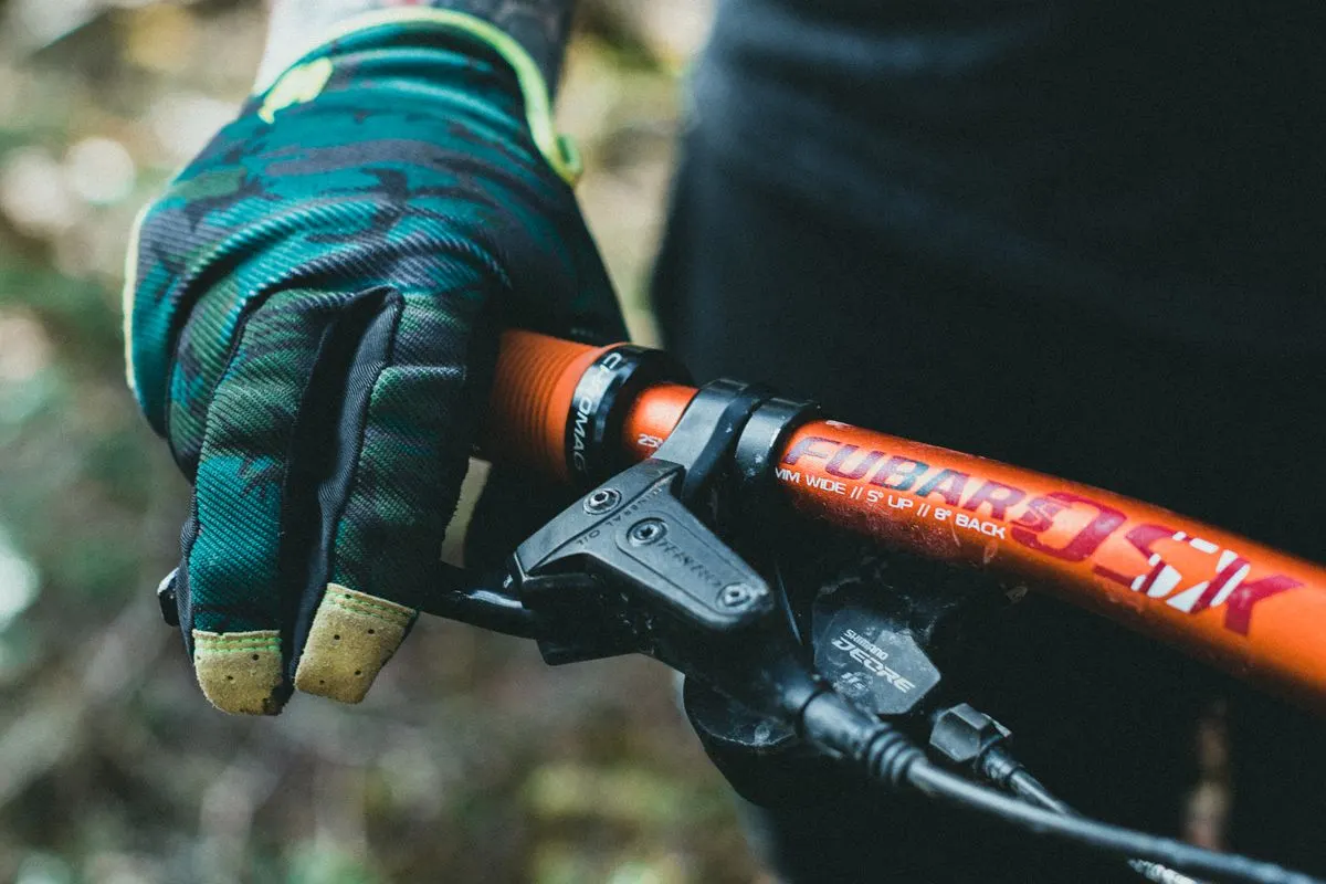 A detailed view of a mountain bike's handlebar with a gloved hand gripping the brake lever.