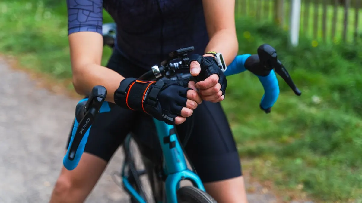 Close-up of a cyclist's hands in black gloves gripping the handlebars of a gravel bike.