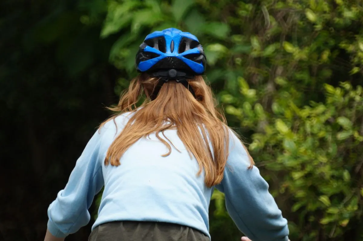 A person in blue attire and helmet cycling outdoors in a green forest area.