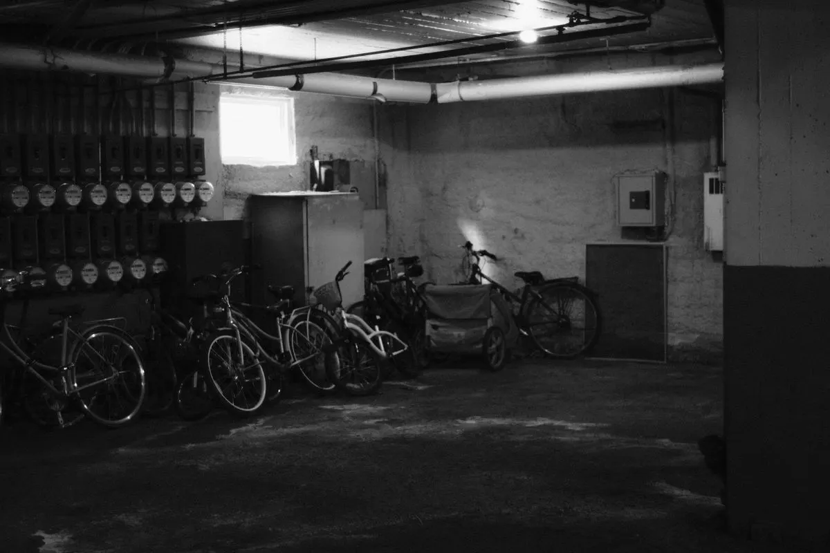 Monochrome image of bicycles stored in an underground basement with industrial fixtures.