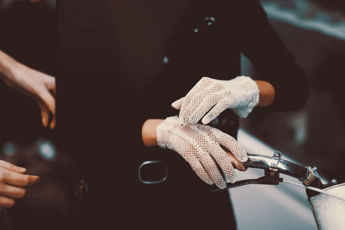 A woman wearing lace gloves holds a vintage bicycle handlebar, exuding elegance.