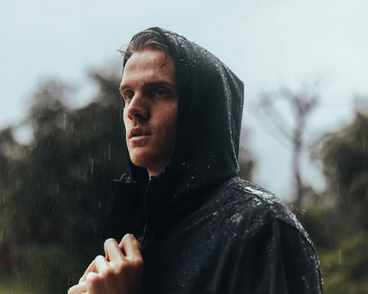 Portrait of a young man in a raincoat outdoors during rainy weather.