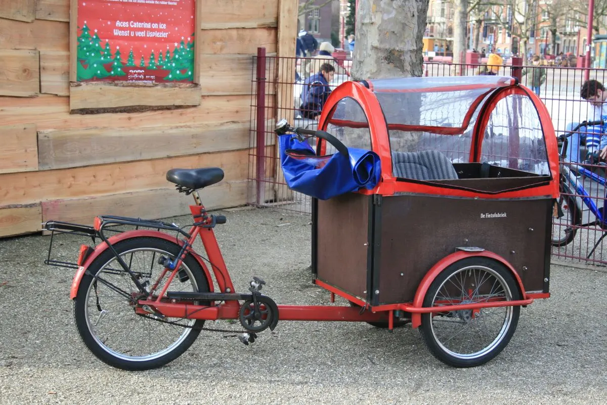 A stationary red cargo bike with a canopy parked on a city street, symbolizing eco-friendly urban transport.