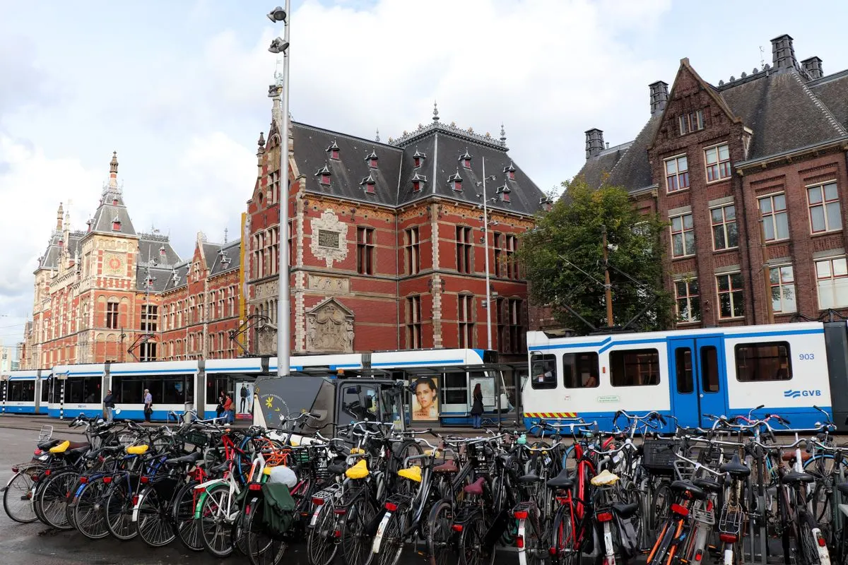 Bicycles parked near trams at Amsterdam Centraal Station on a busy day.