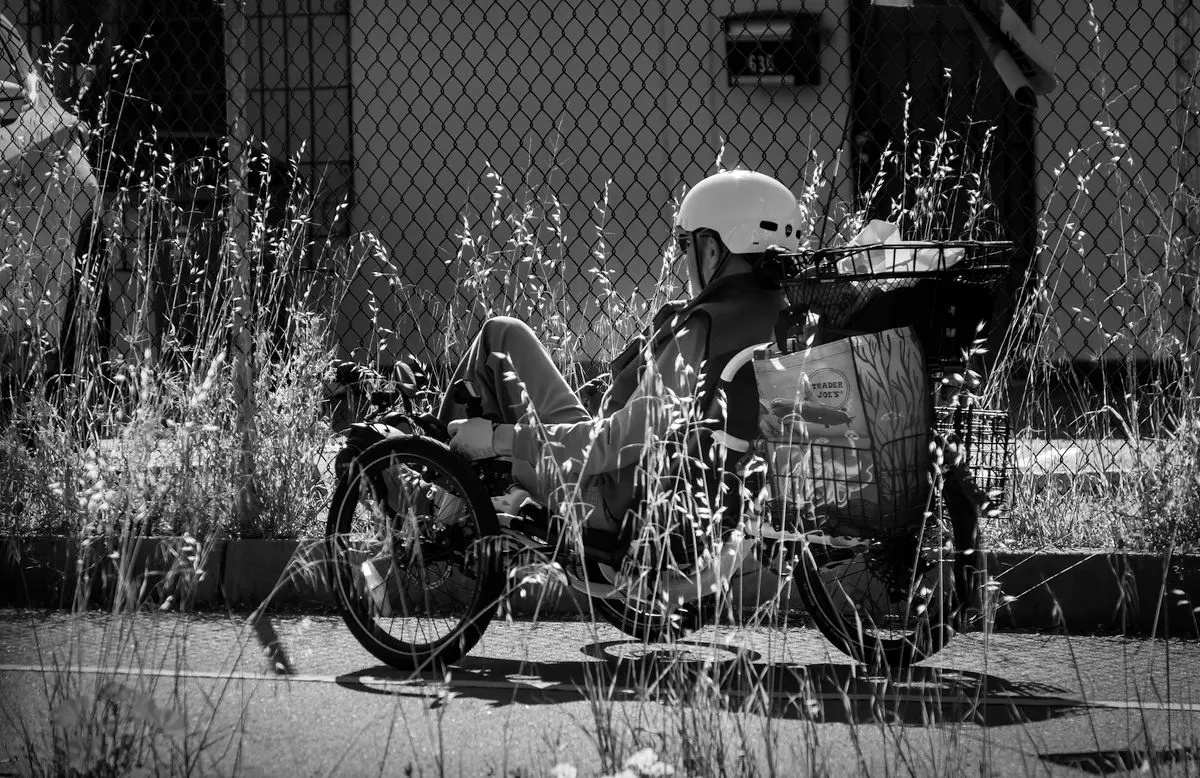 Black and white image of a cyclist riding a recumbent bike on a city street.
