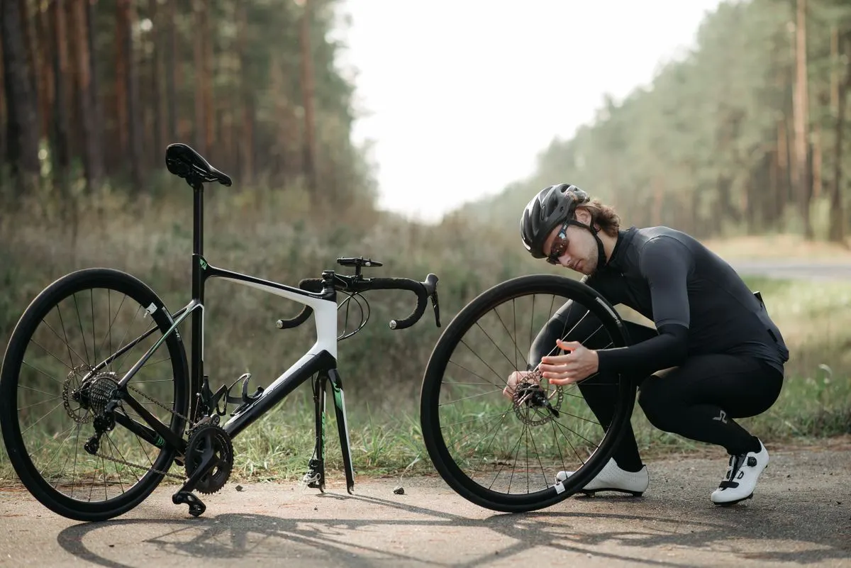 Cyclist fixing a road bike wheel on a forest path during daytime.