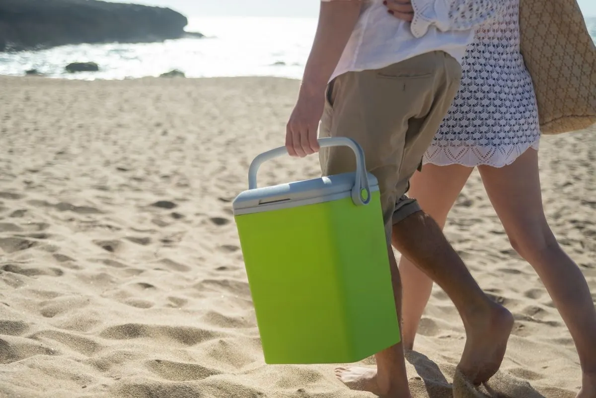 A couple walks along a sunny beach in Portugal carrying a cooler.